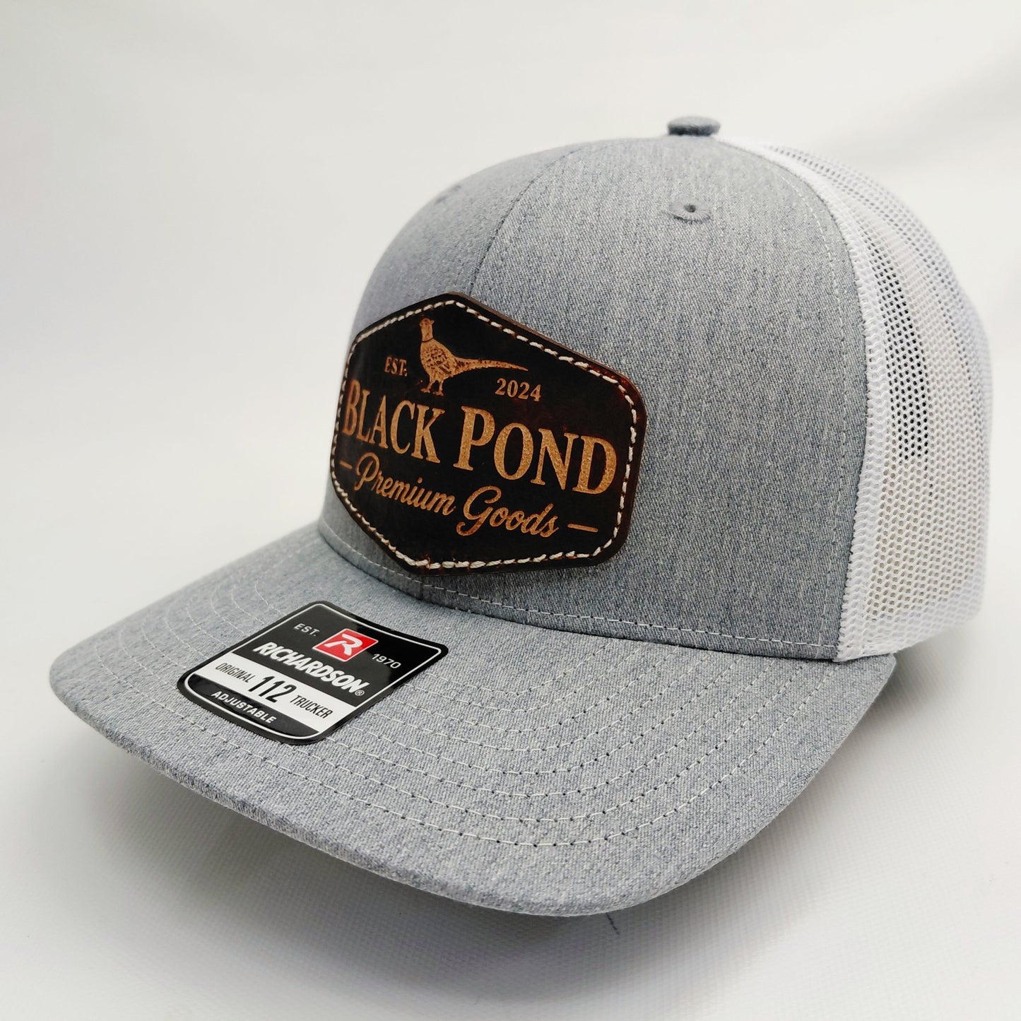 Left angled view of Black Pond pheasant leather patch Richardson 112 trucker hat in heather gray and white