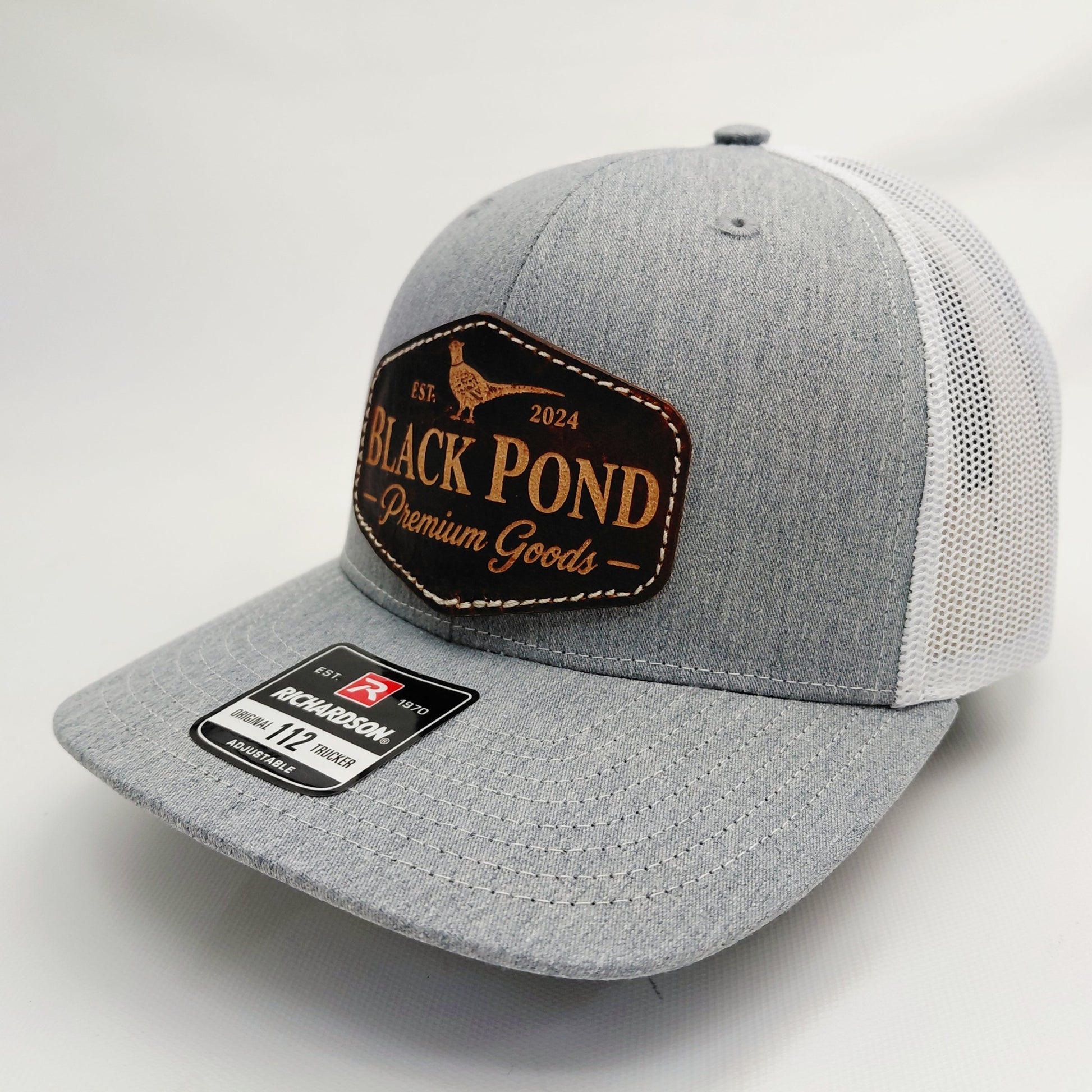 Left angled view of Black Pond pheasant leather patch Richardson 112 trucker hat in heather gray and white