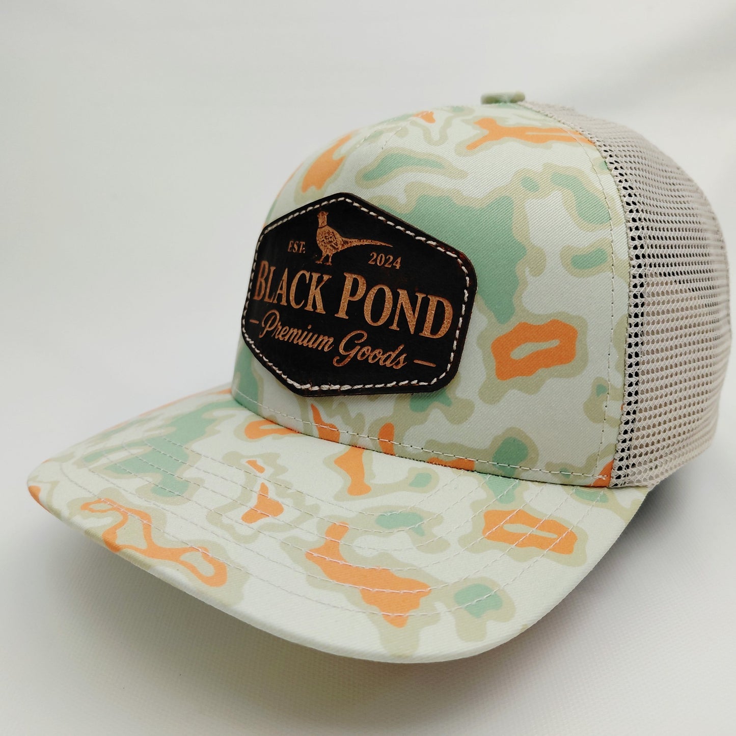 Left angled view of Black Pond pheasant leather patch Richardson 112 mint orange camouflage trucker hat