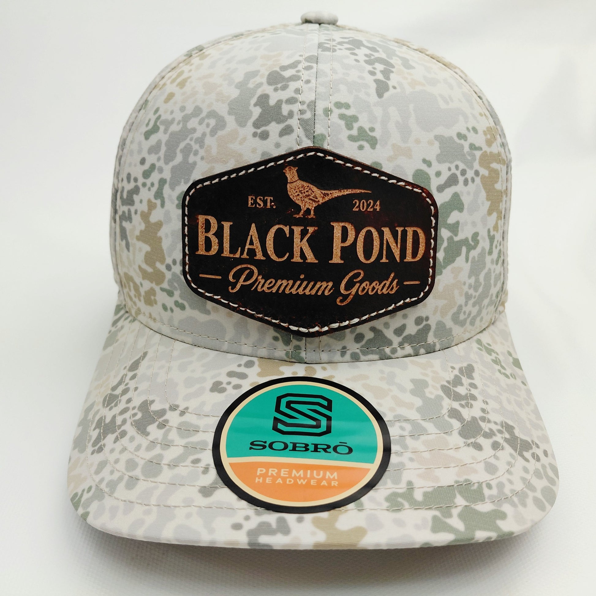 Front view of Black Pond pheasant leather patch SOBRO perforated trucker hat in multicolor camouflage