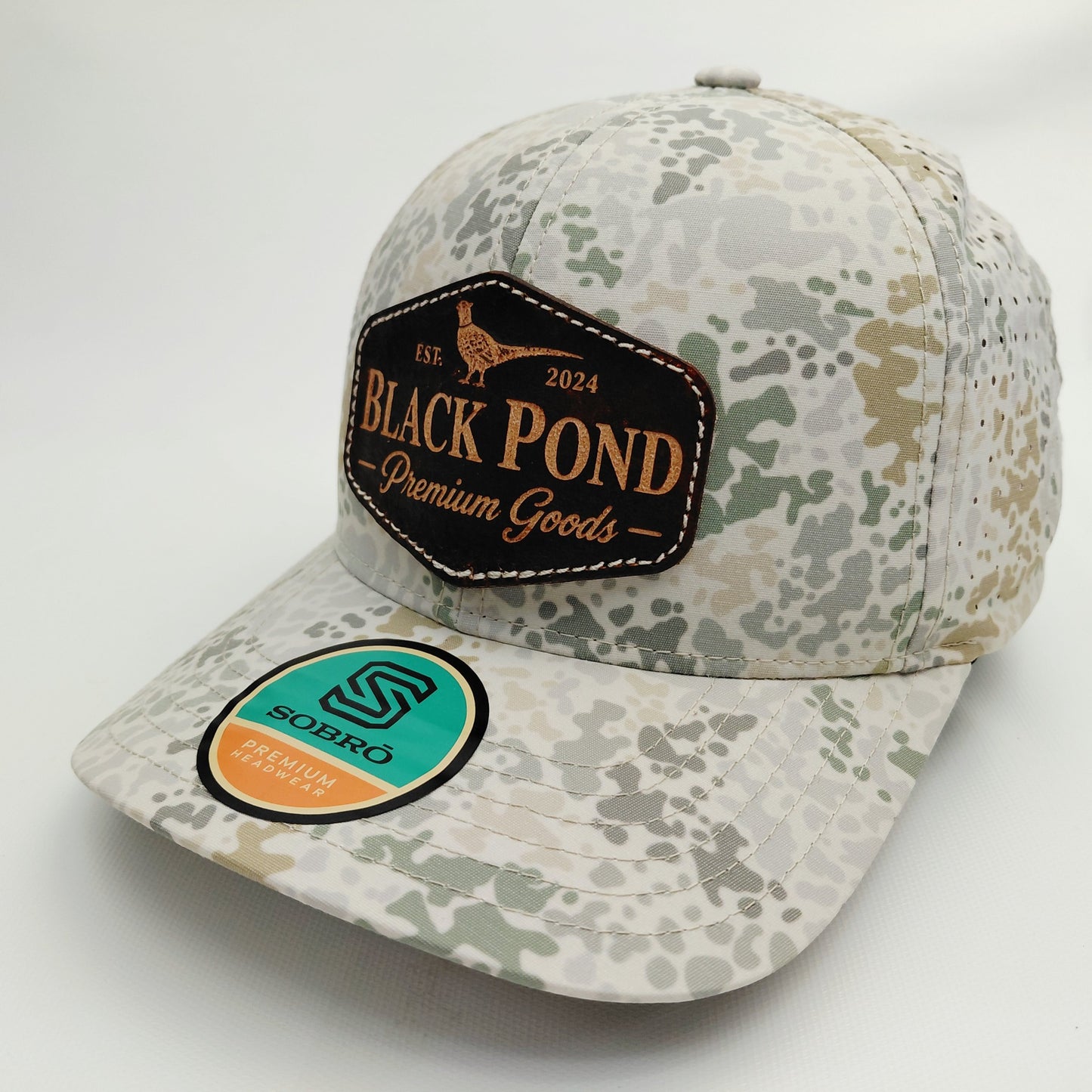 Left angled view of Black Pond pheasant leather patch SOBRO perforated camouflage trucker hat