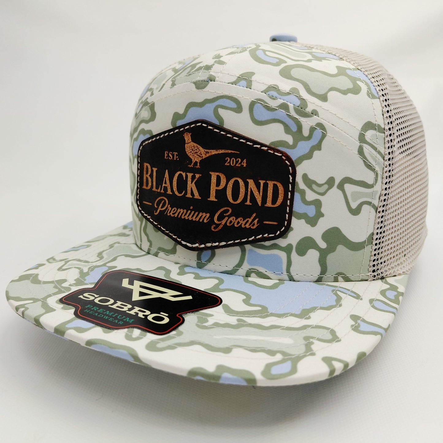 Left angled view of Black Pond pheasant leather patch SOBRO seven-panel camouflage trucker hat