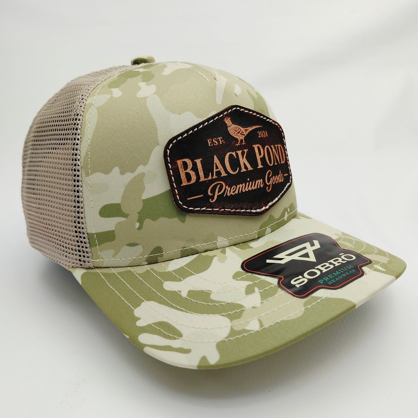 Right angled view of Black Pond pheasant leather patch SOBRO seven-panel tan camouflage trucker hat